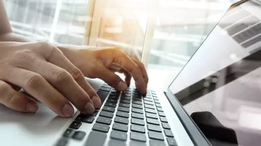 Manos escribiendo en un teclado de computadora iluminada por la luz.